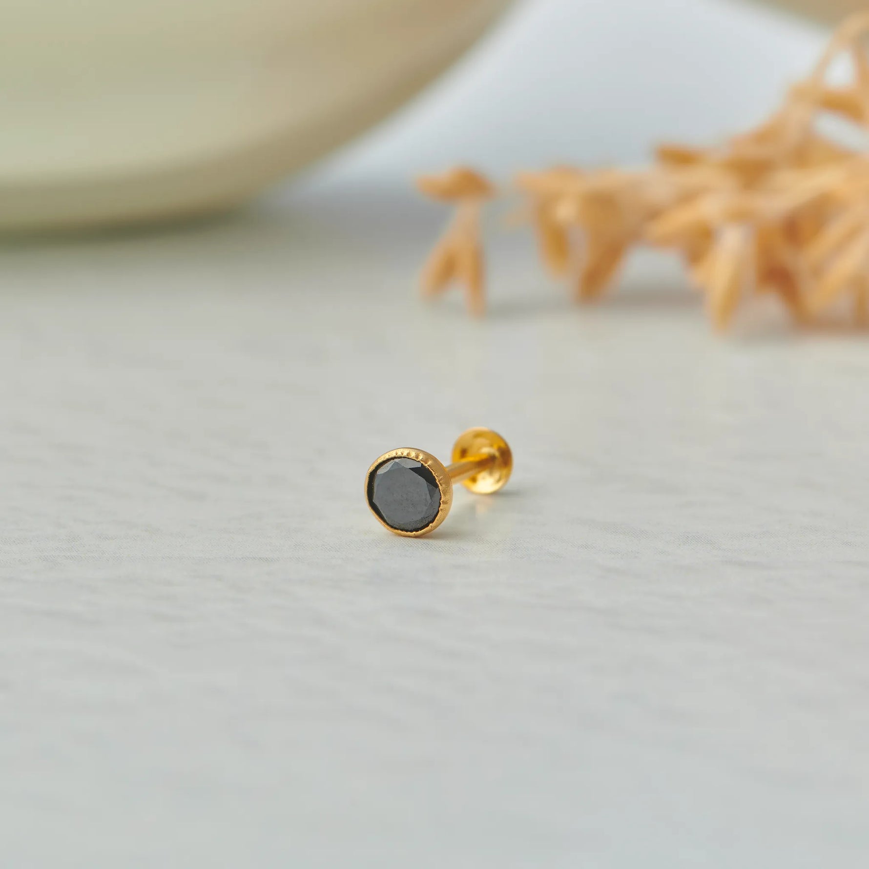 Gold nose pin with black gemstone placed on a light surface