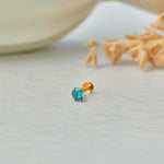 Gold stone nose pin with blue gemstone placed on a light surface