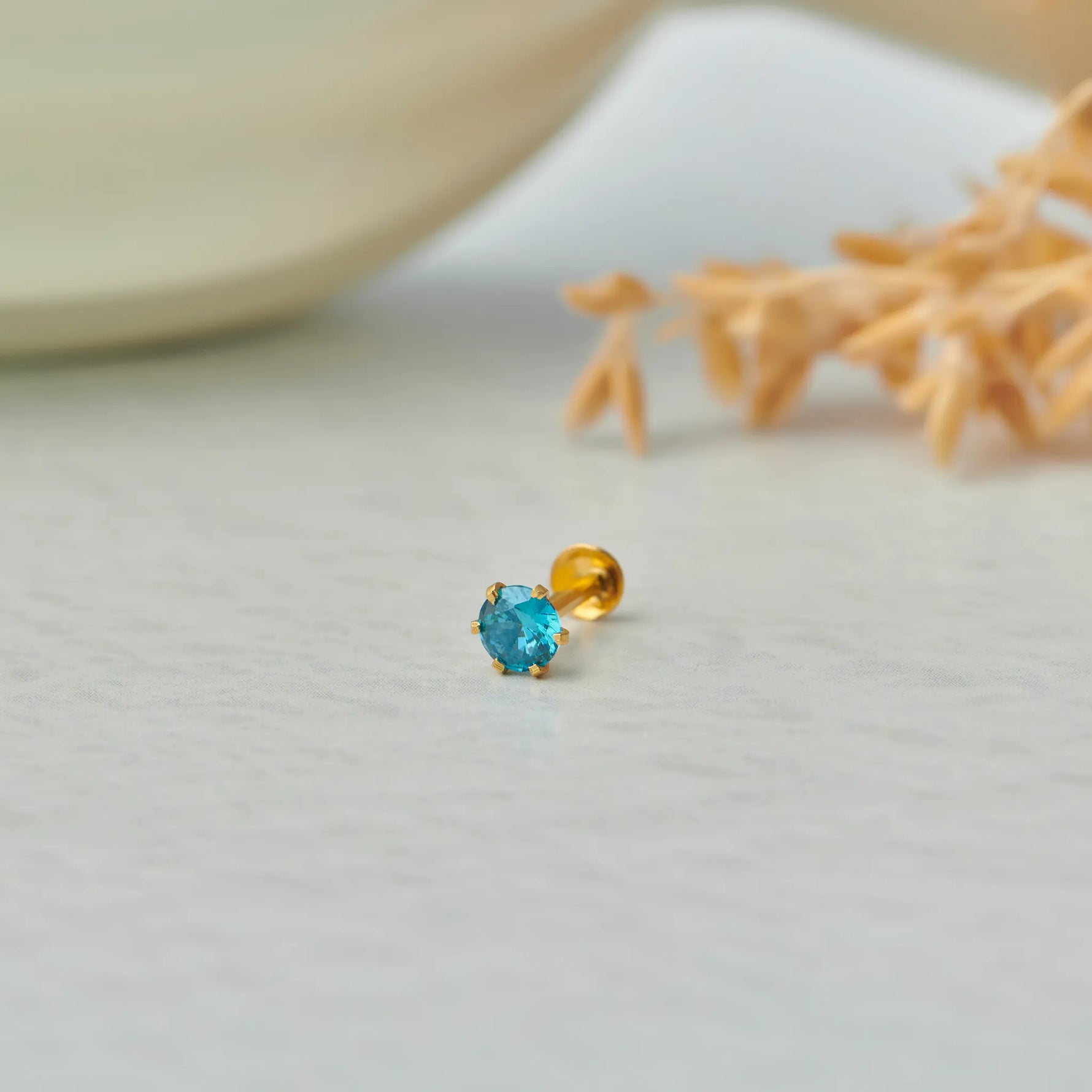Gold stone nose pin with blue gemstone placed on a light surface