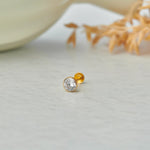 Gold stone nose pin with clear gemstone placed on a light surface