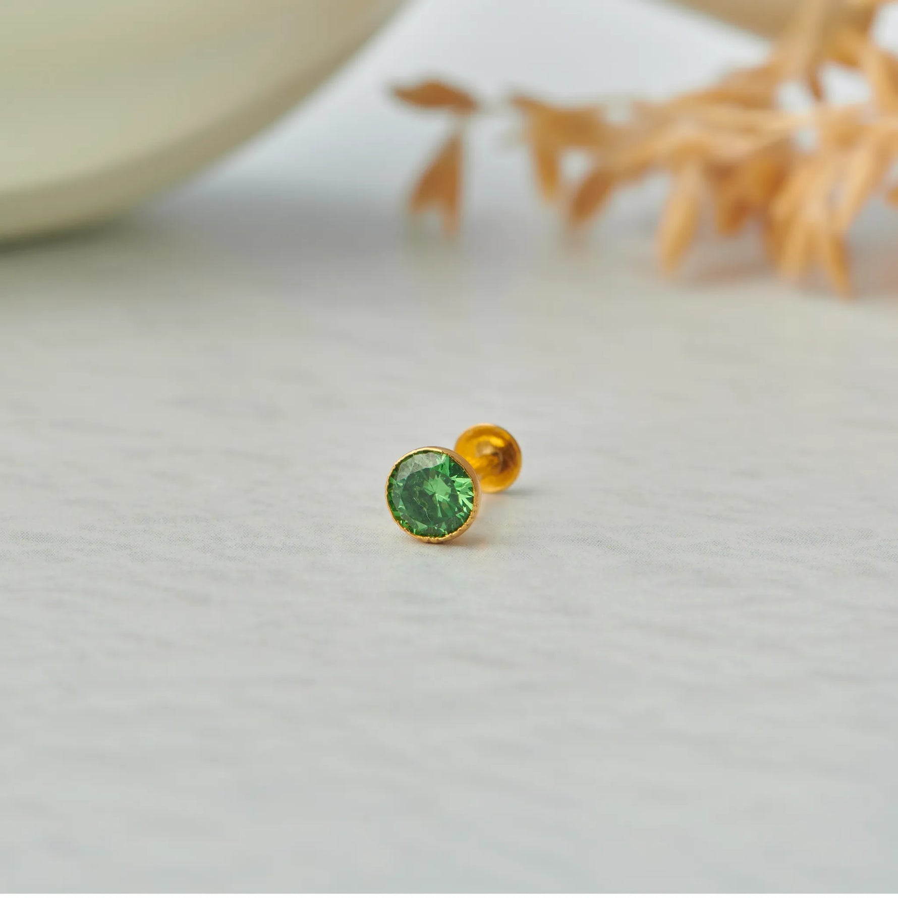 Gold stone nose pin with green gemstone placed on light surface