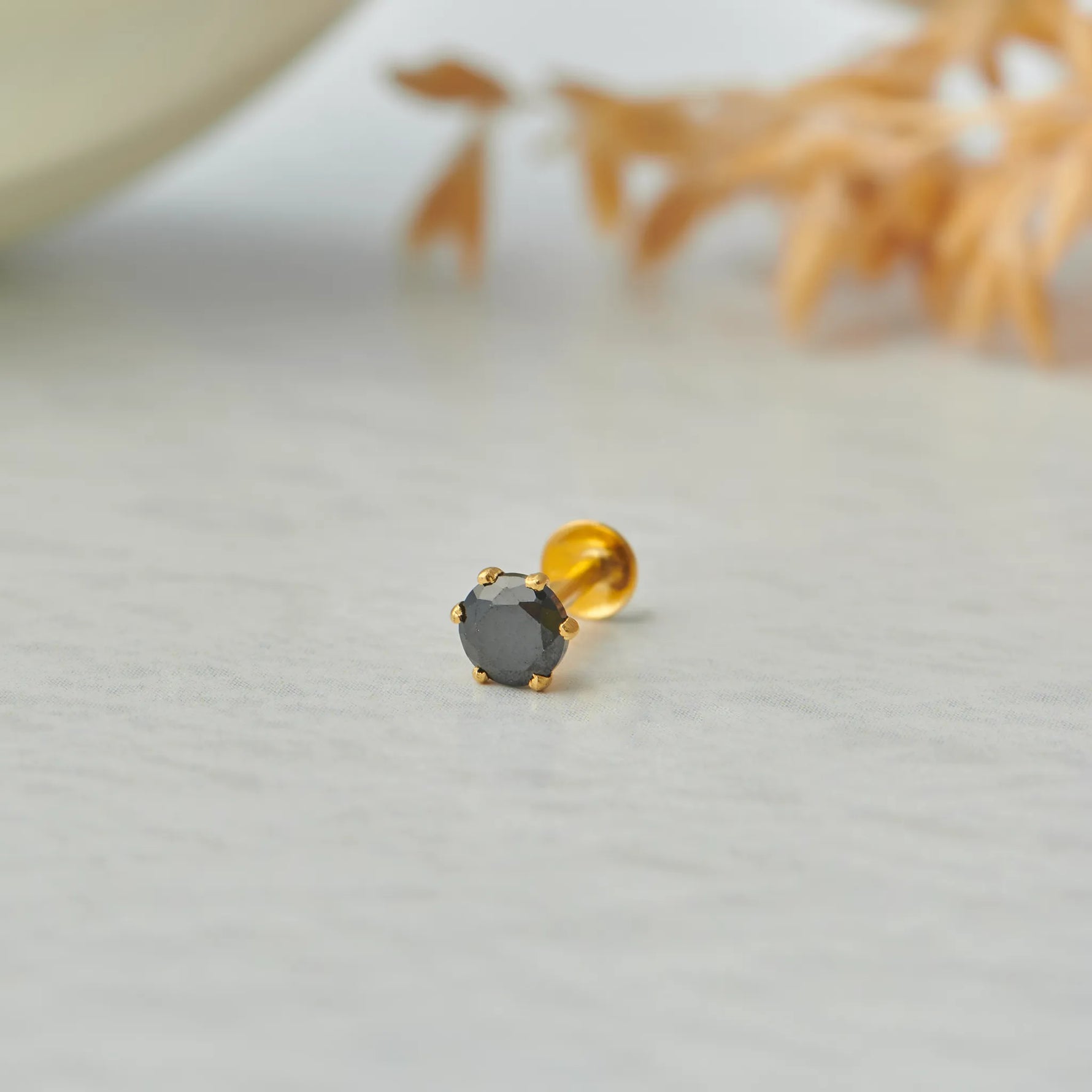 Close up of single black stone gold nose pin on white surface