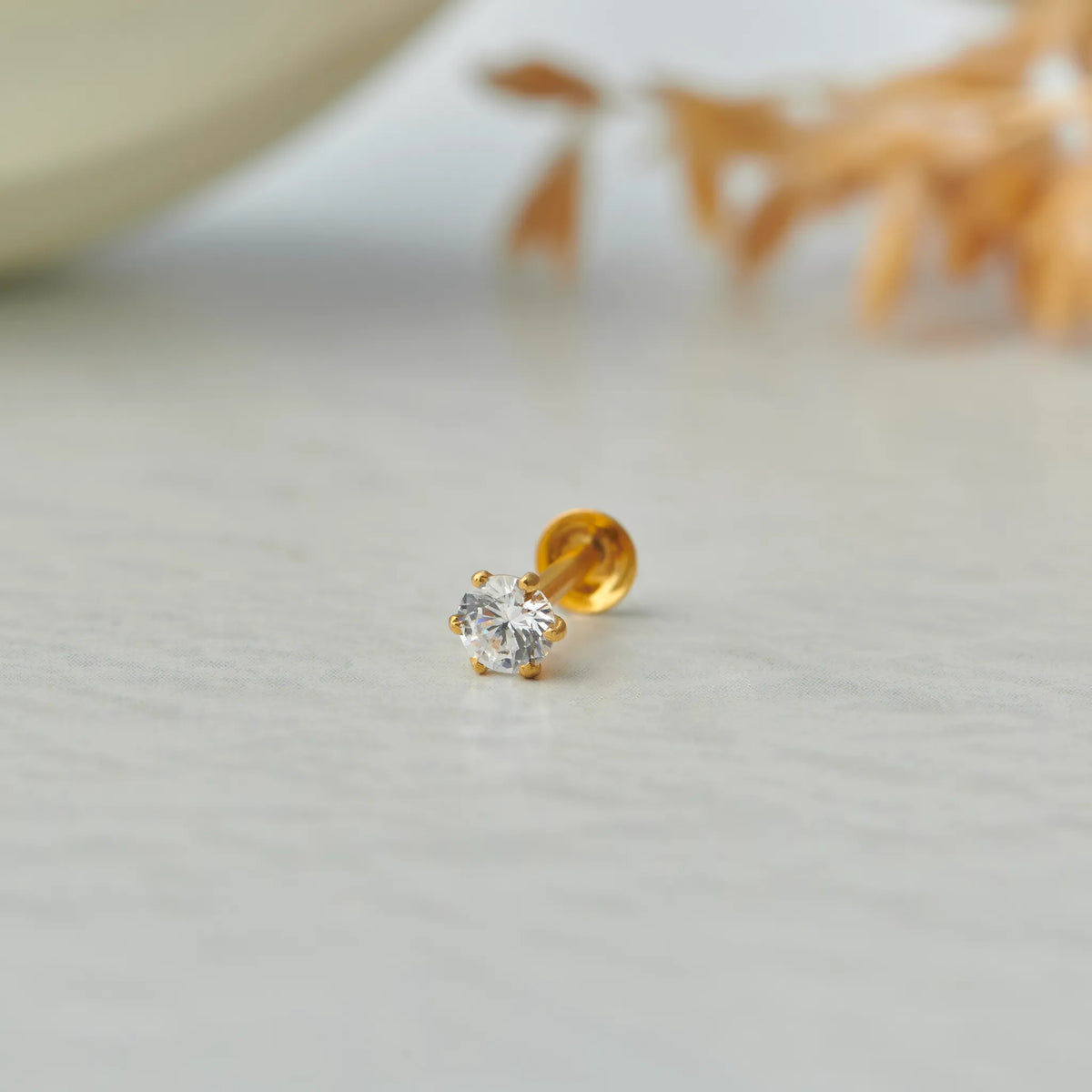 Close up of single white stone gold nose pin placed on a light textured surface with soft decor in background