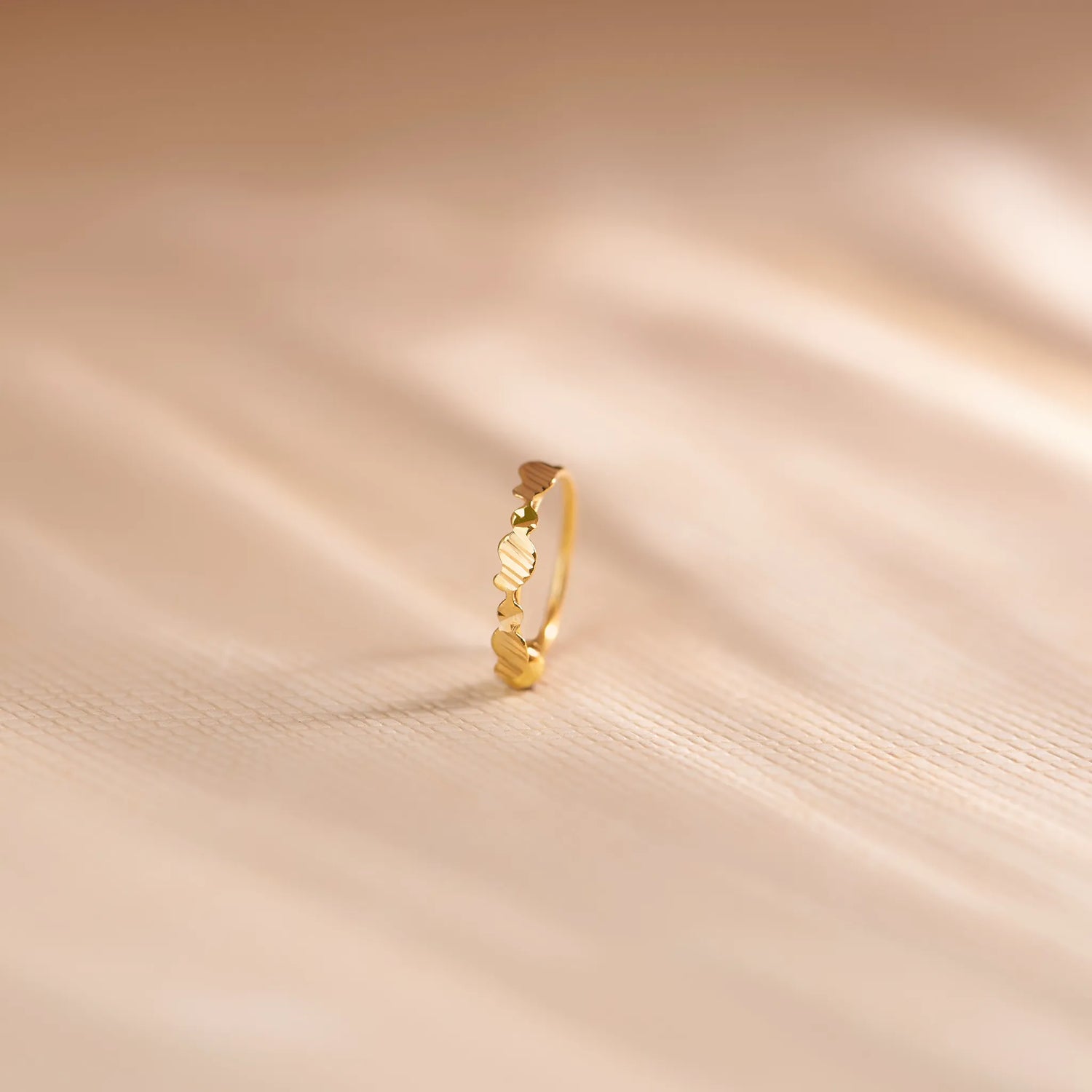 Close up of an 18K gold nose ring with delicate openwork swirl design standing upright on a soft beige textured background with warm light shadows