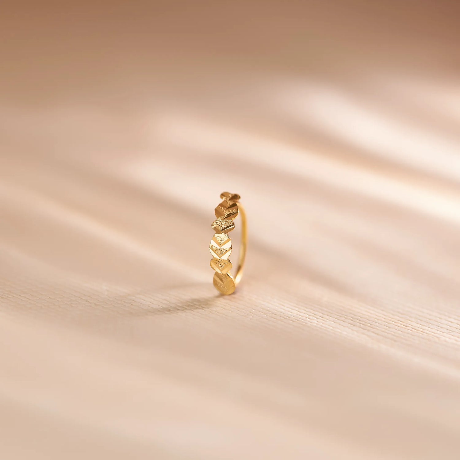 Close up of twisted pattern 18K gold nose ring standing upright on a soft beige textured background